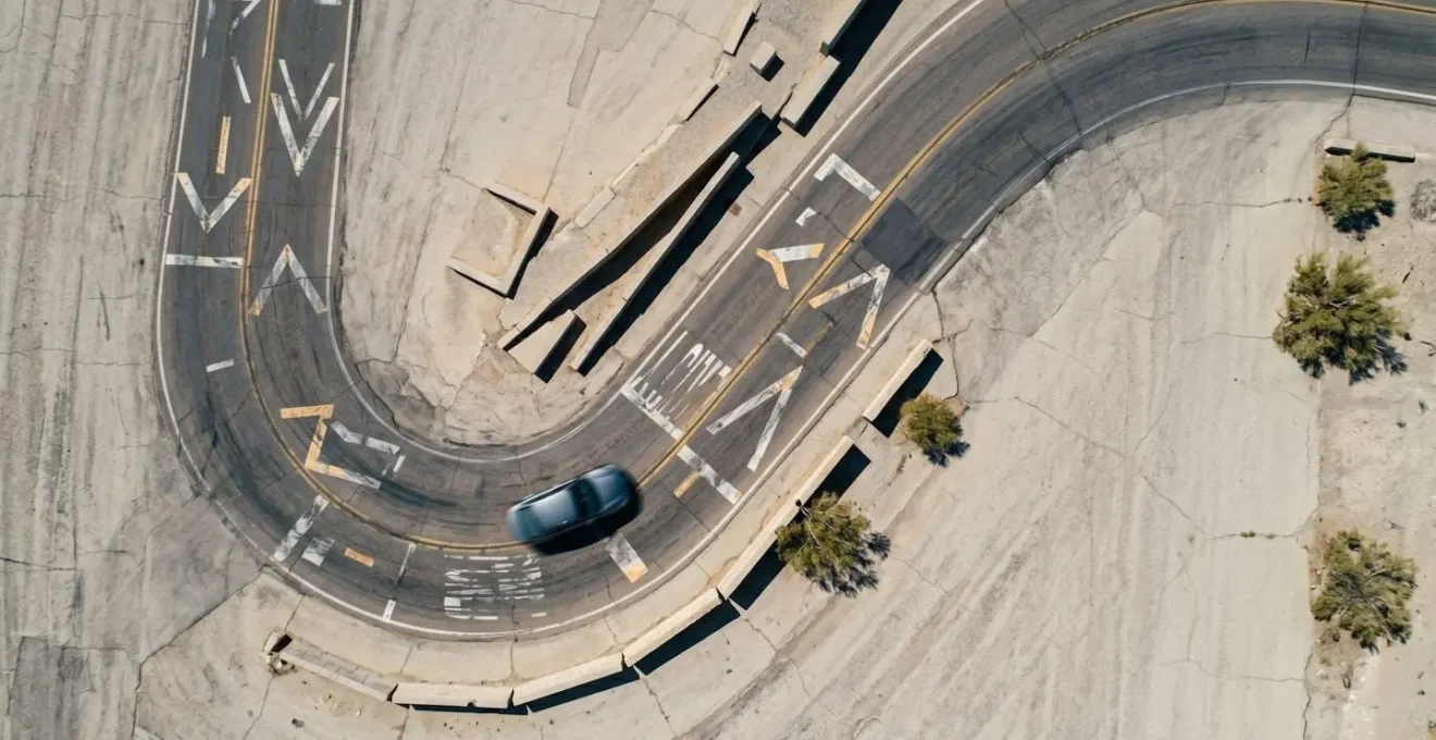 Vue aérienne minimaliste d'une route sinueuse avec une voiture en mouvement et des marquages au sol abstraits